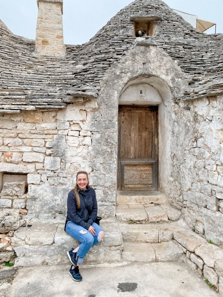 jillian, travel and wellness influencer, sitting in front of a trulli in Alberobello in Puglia, Italy