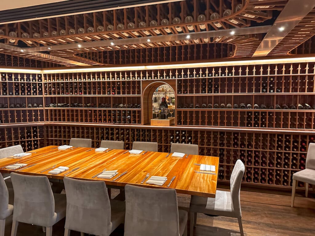 The wine room at Brix in Napa Valley features an elegant dining table surrounded by shelves filled with an extensive collection of wine bottles. The warm wooden tones of the shelves and table create a cozy yet sophisticated atmosphere, perfect for a refined dining experience.